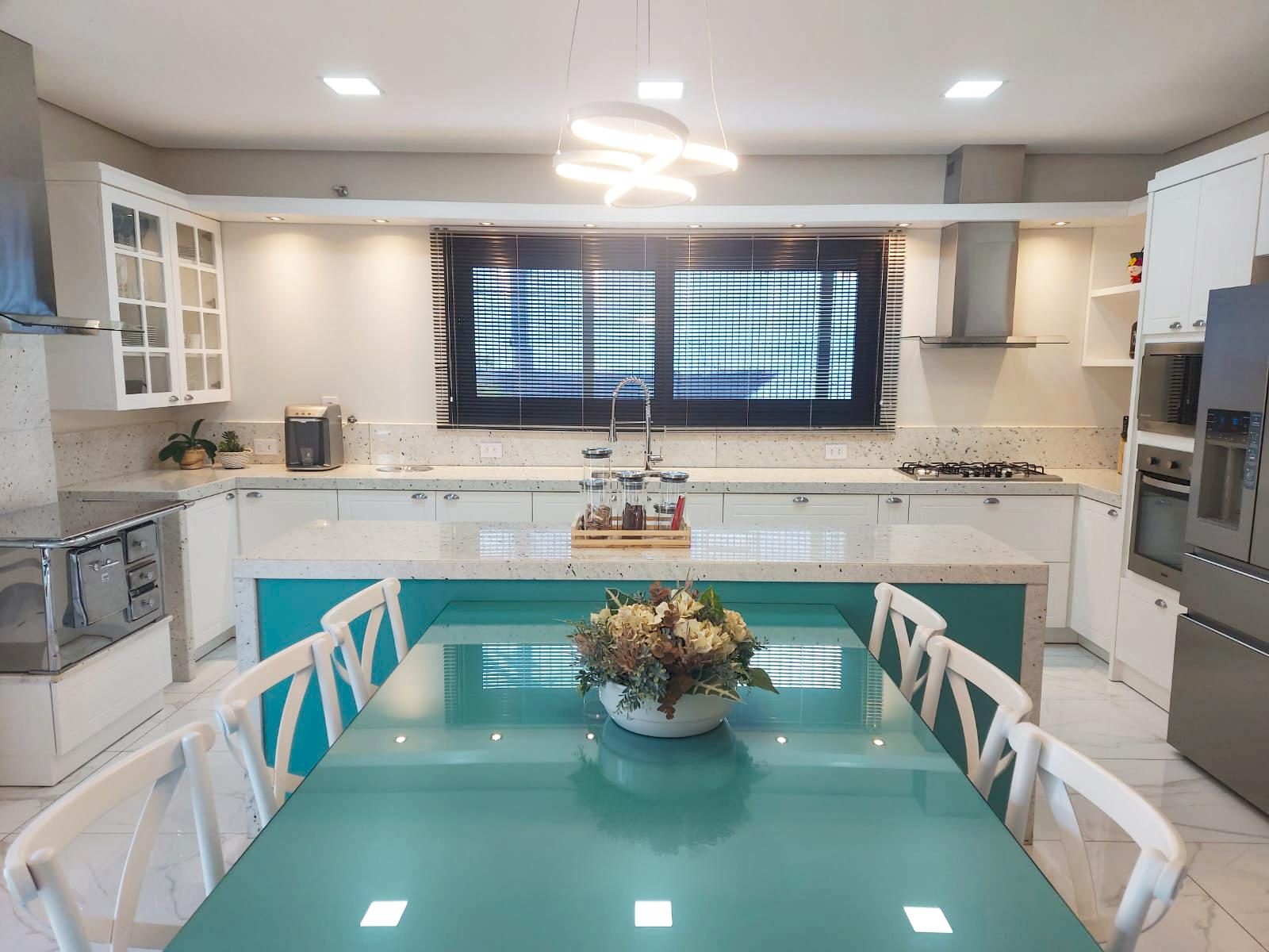 Cozinha ampla planejada com ilha verde-água e mesa de vidro