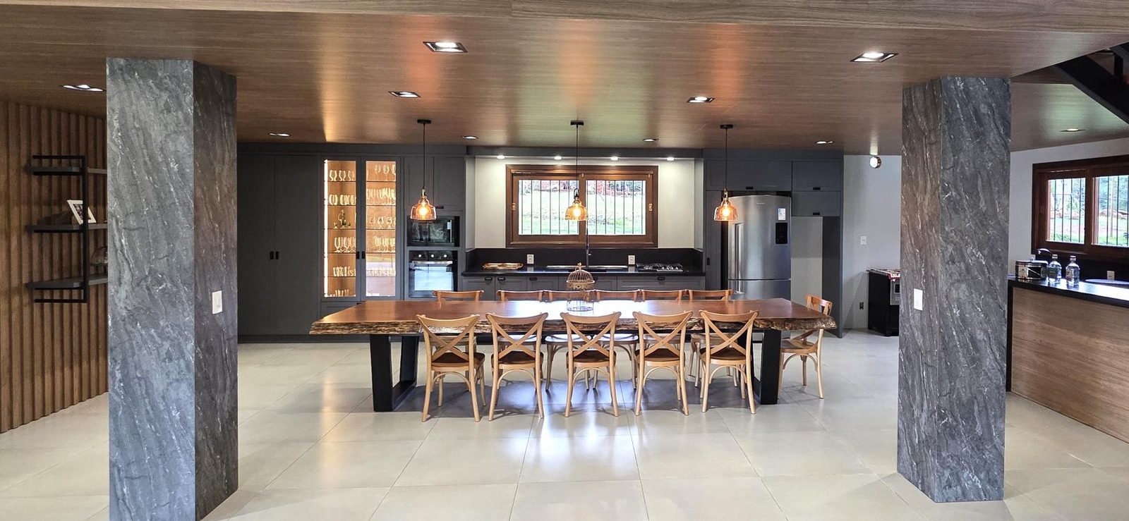 Cozinha integrada planejada com mesa grande de madeira e armários grafite