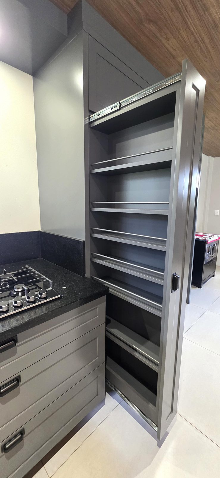 Armário despenseiro planejado com prateleiras deslizantes ao lado do cooktop
